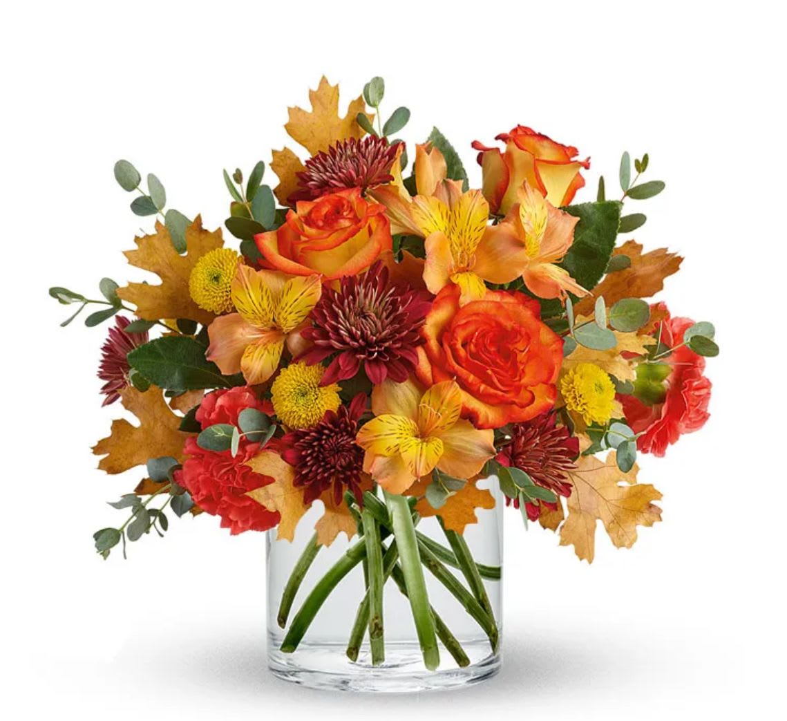 Autumn bouquet of orange roses and mixed flowers in a clear glass vase