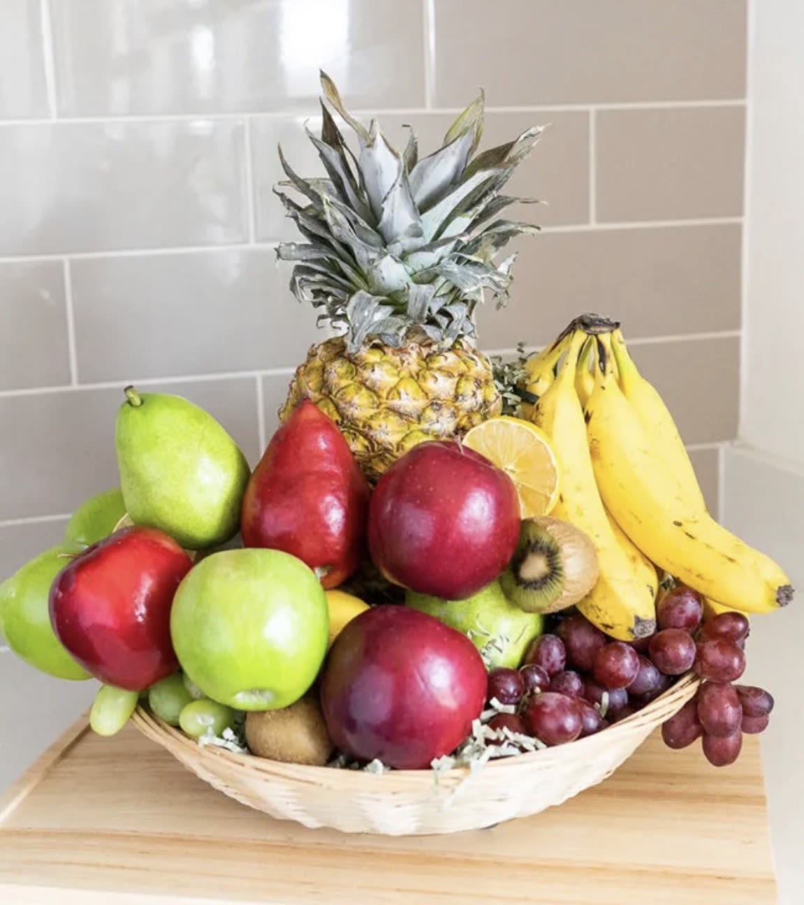 Basket of assorted fruit with pineapple, bananas, grapes, apples, and kiwi