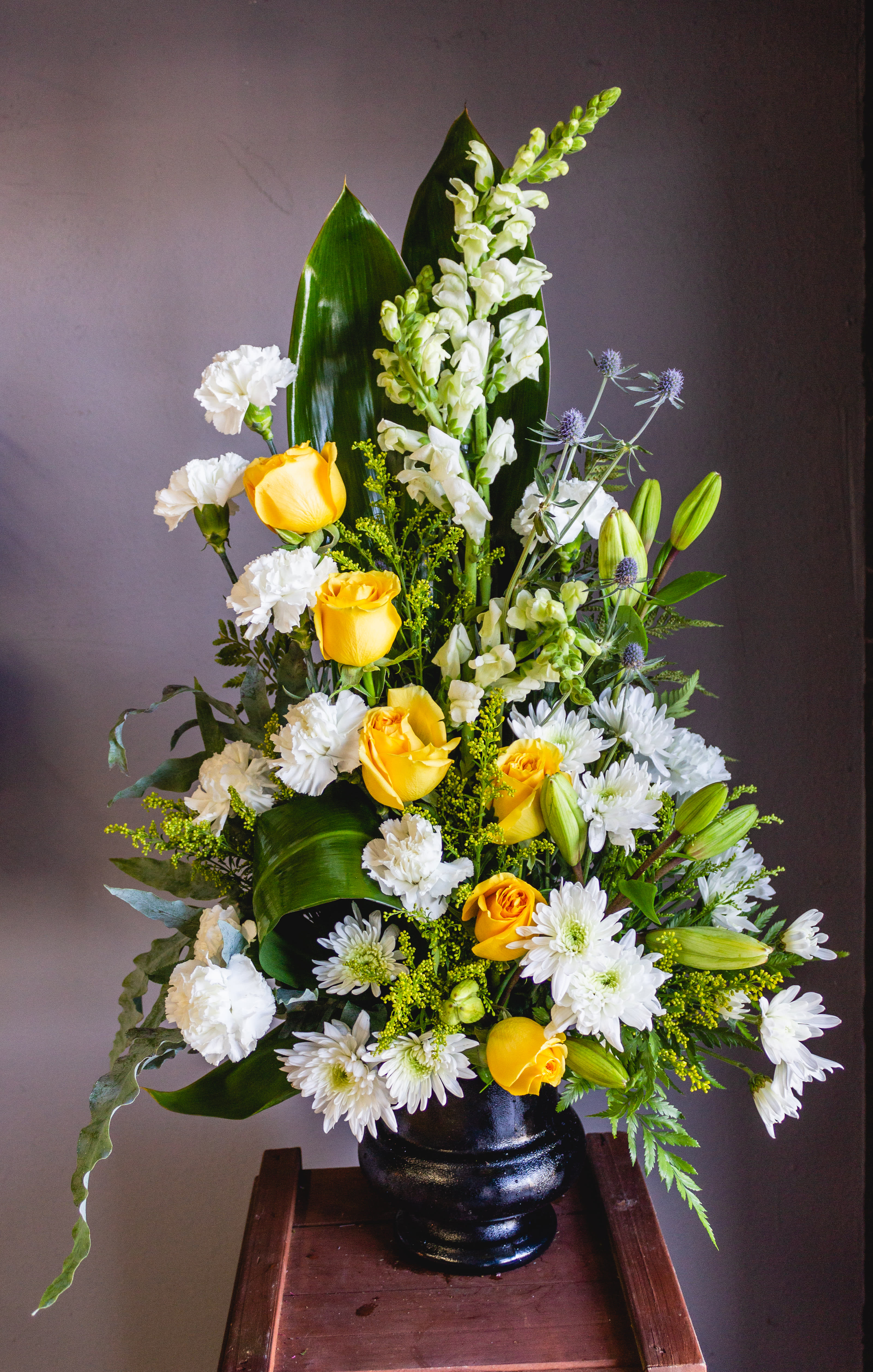 Tall floral arrangement with yellow roses, white blooms, and a black vase