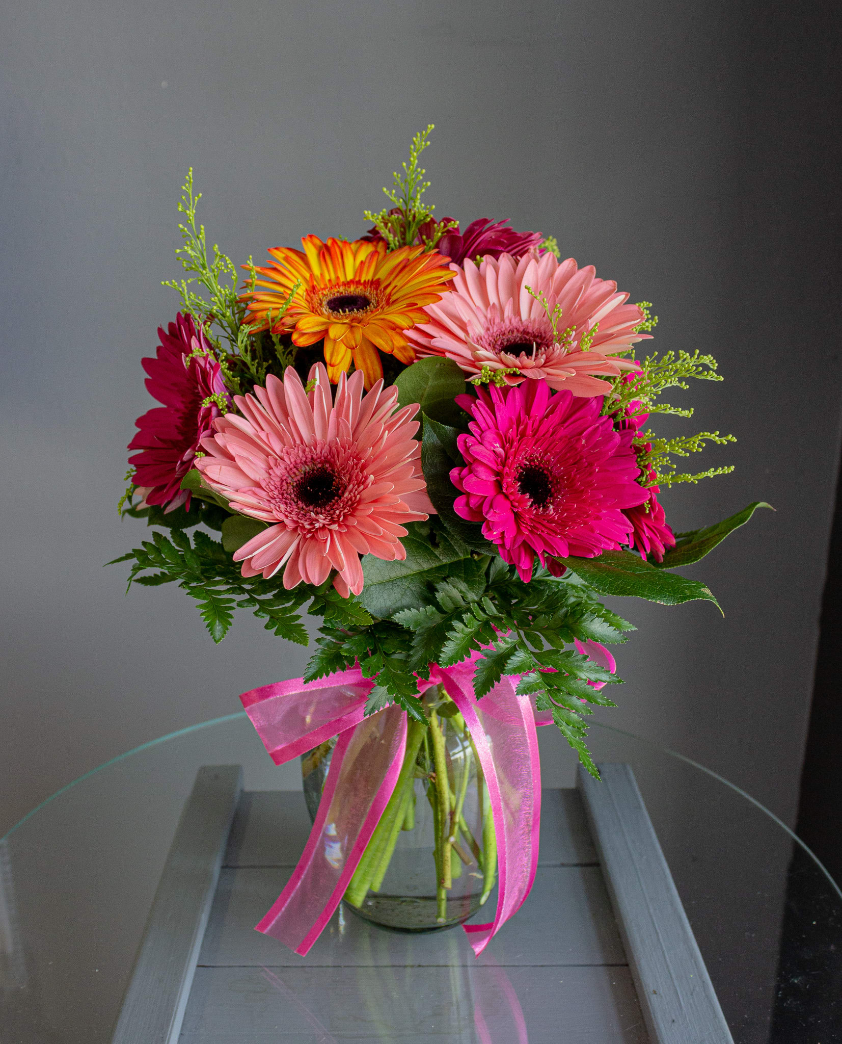 Dozen Gerbera - A lovely, cheerful mix of a dozen gerbera daisies and greens in a vase. The colors will vary based on what is freshest and will be a mix of color