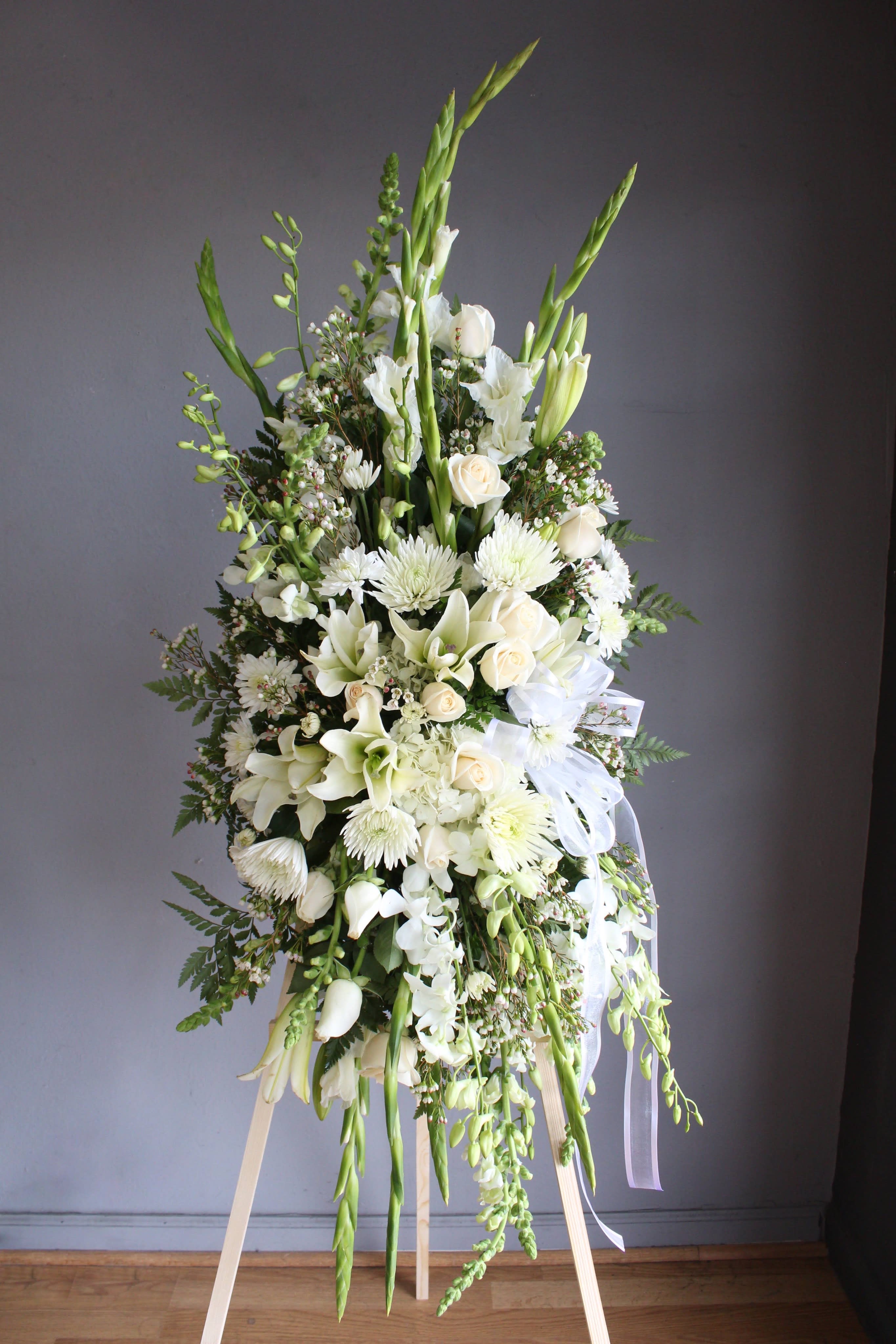 Tall white floral standing spray with lilies, roses, and ribbons