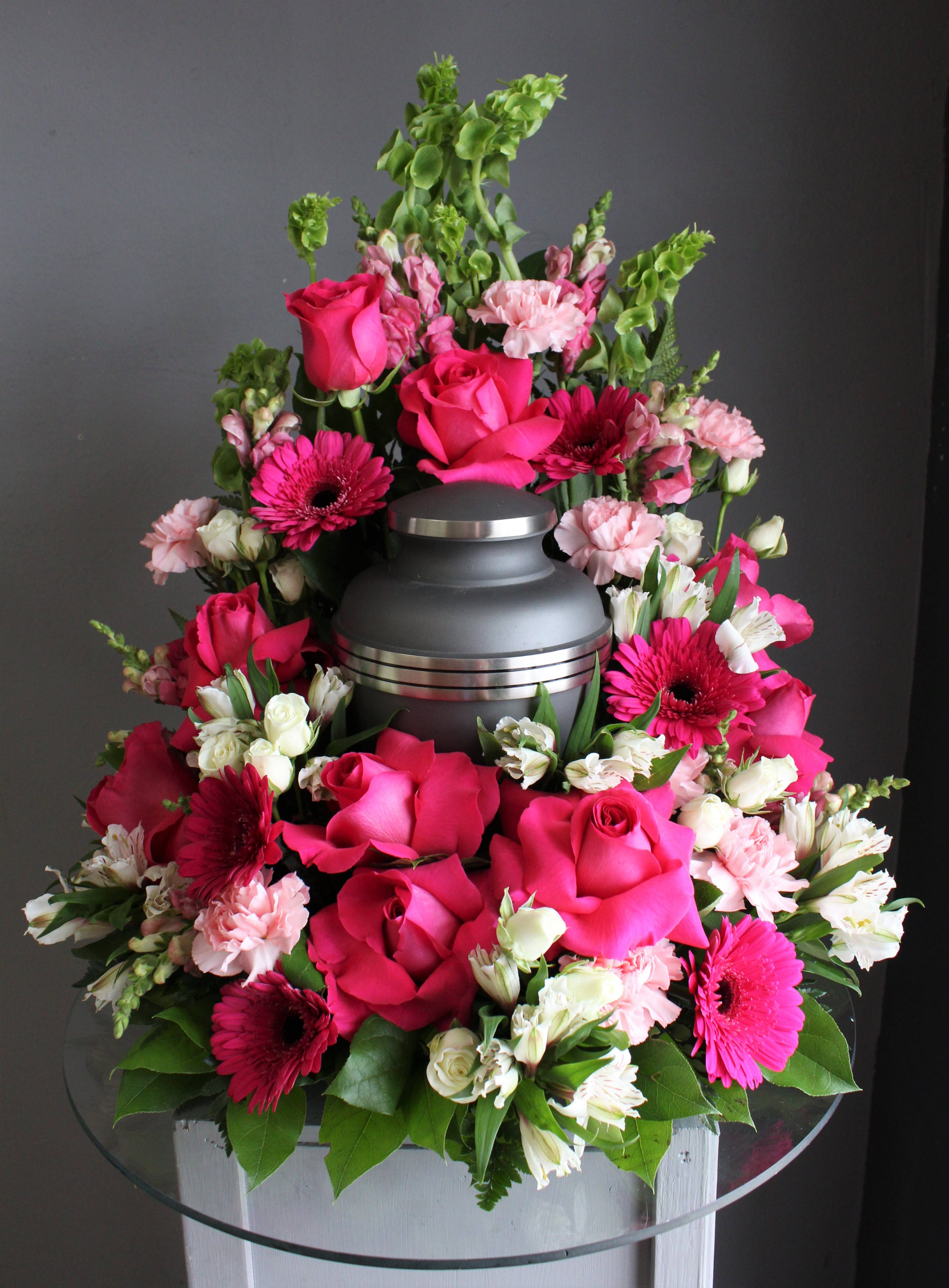 FUNERAL URN WREATH - Pink Abundance 66 - This is a beautiful option for a memorial service with soft colors. This open ring wreath will be designed with a 10.5” ring form with the urn resting in the middle. This piece features pink and white flowers with a feminine look from flowers like roses, gerber daisies, snap dragons and bells of Ireland. This is a great option for a cremation service to surround your loved one in the beauty of pink and white.   **This is a piece for a funeral or memorial service. Please place the order at least 2 days prior to the service to guarantee a certain arrangement. Anything sooner and we cannot guarantee it will match the picture. These pieces can be customized to the color of your choice. The flowers may vary depending on availability of the flowers, special requests and quality of the flowers we have in stock. If you have a special request please add it to our special instructions when placing your order. If you have any questions please don’t hesitate to call. 714 289 1123**