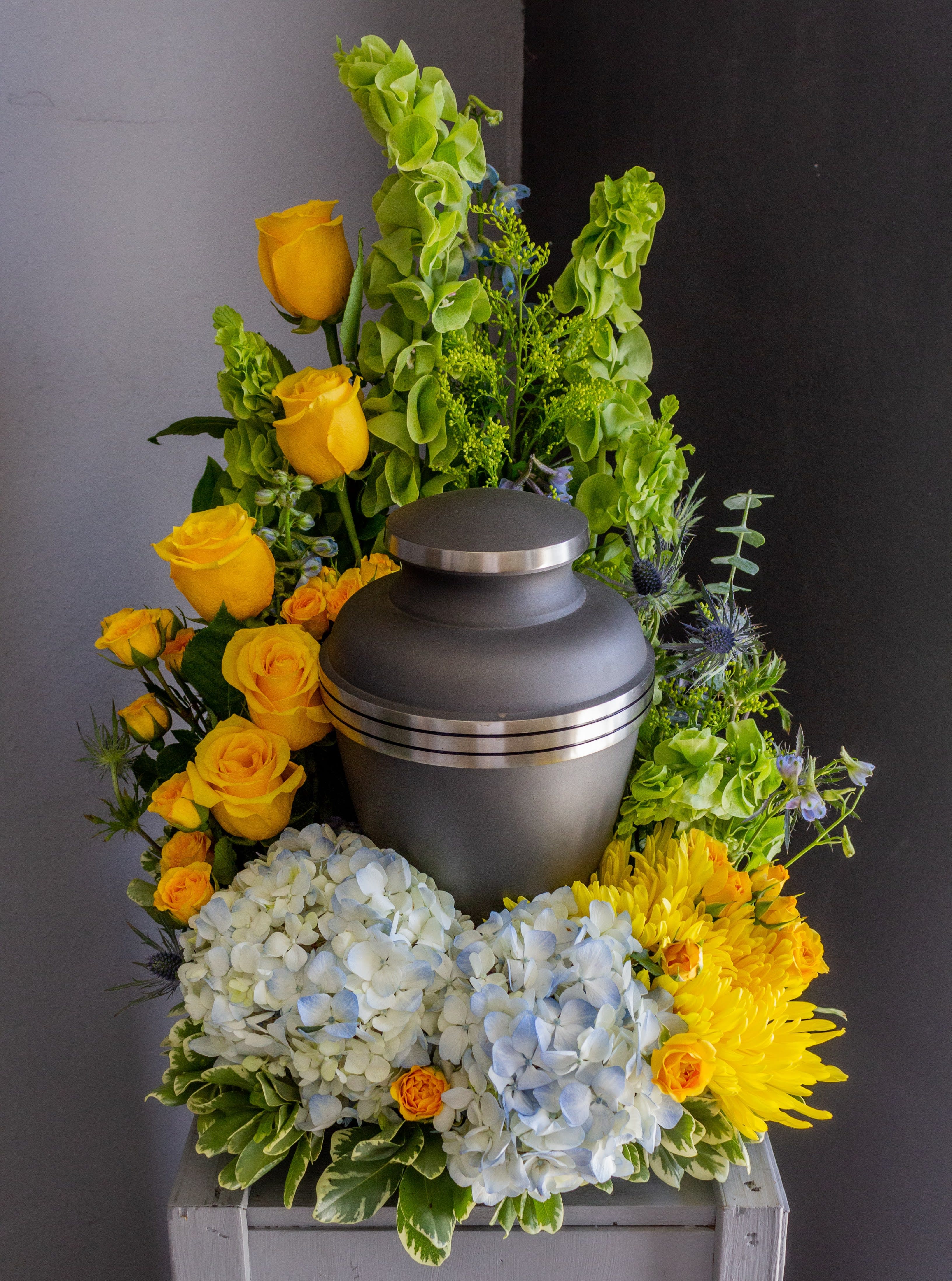 Funeral urn surrounded by yellow roses, hydrangeas, and chrysanthemums