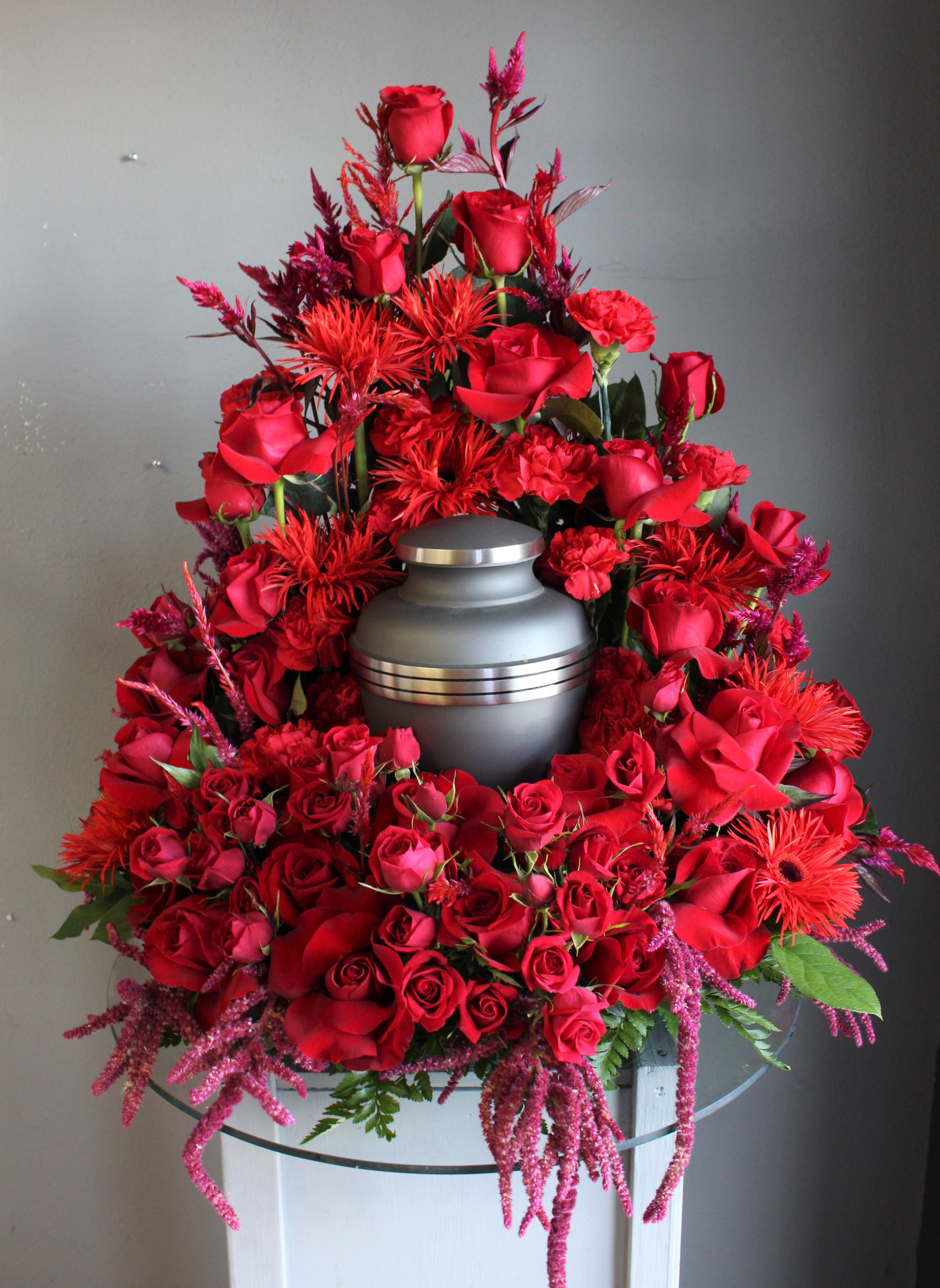 Red rose funeral arrangement around a gray urn