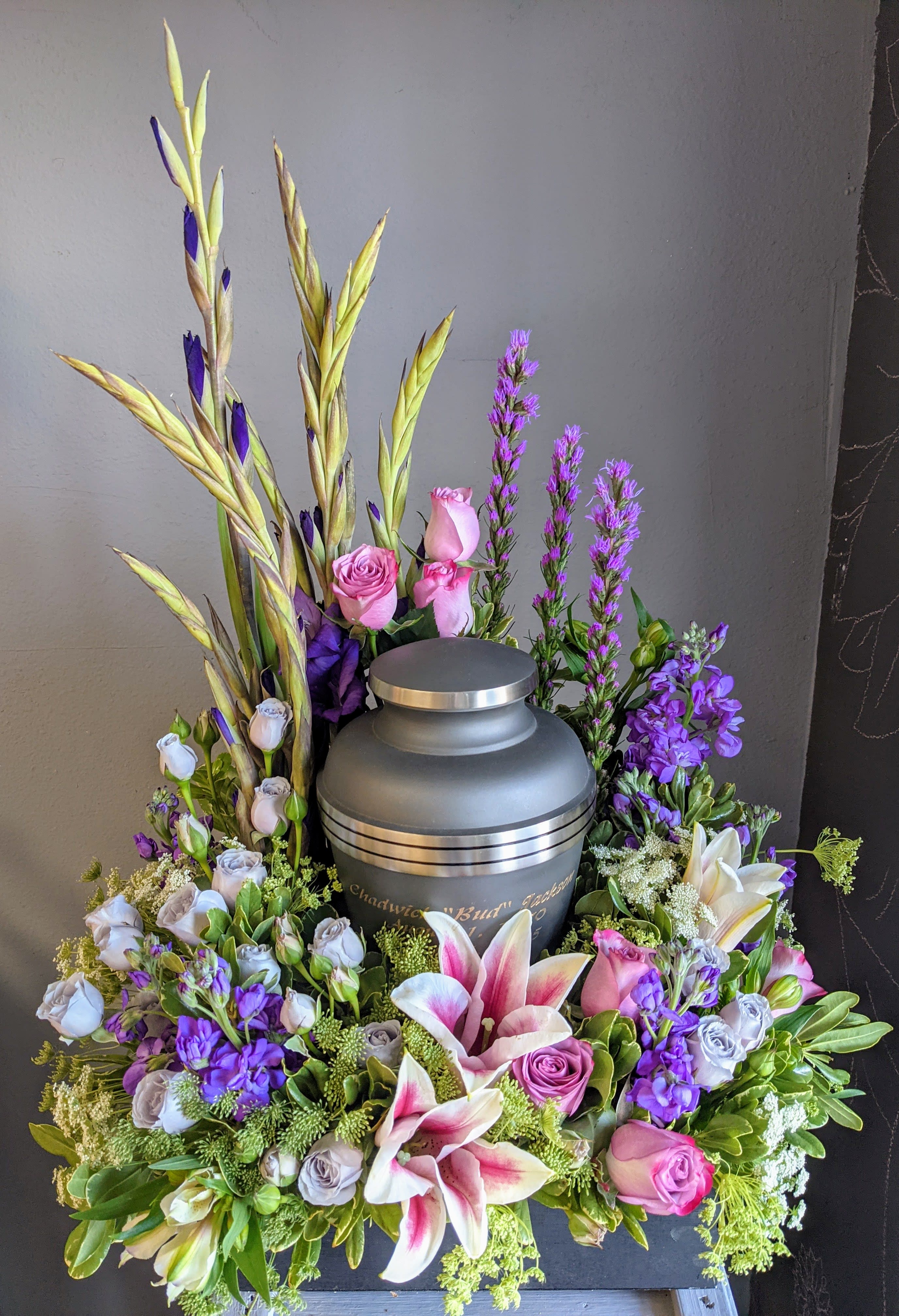 Floral urn arrangement with pink lilies and roses around a gray cremation urn