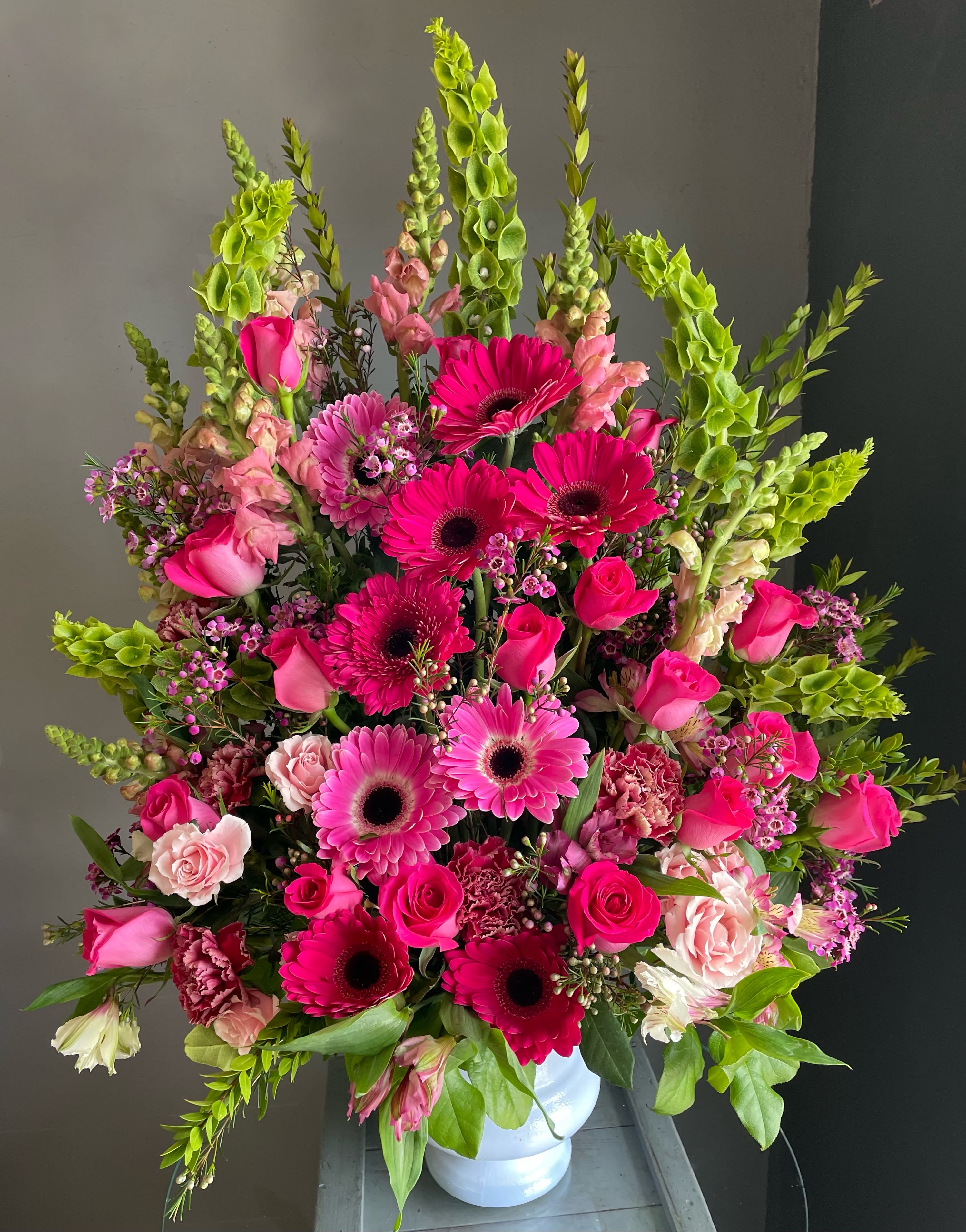 Large pink and green floral arrangement in a white vase