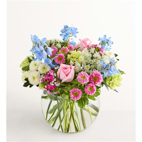 Mixed bouquet of pink roses, blue flowers, and daisies in a clear glass vase