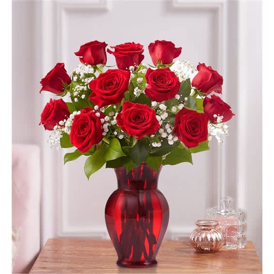 Red roses arranged in a red glass vase with white filler flowers