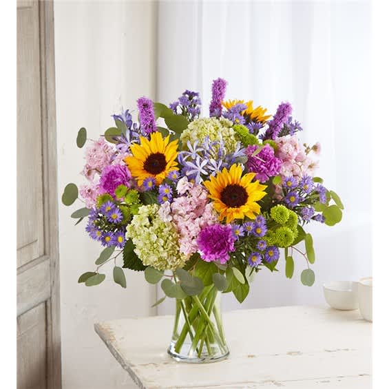 Mixed bouquet with sunflowers, purple blooms, and pink flowers in a glass vase