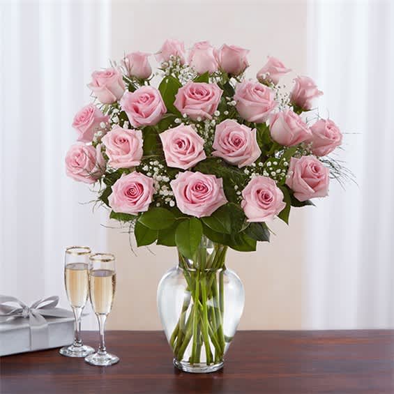 Pink roses in a clear glass vase with two champagne flutes and a gift box