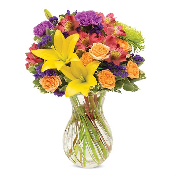 Mixed bouquet of yellow lilies, orange roses, and pink flowers in a clear glass vase