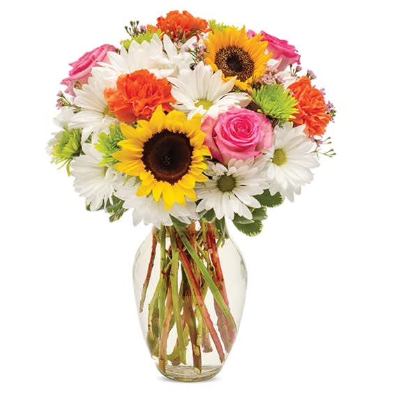 Mixed bouquet of sunflowers, daisies, roses, and carnations in a glass vase