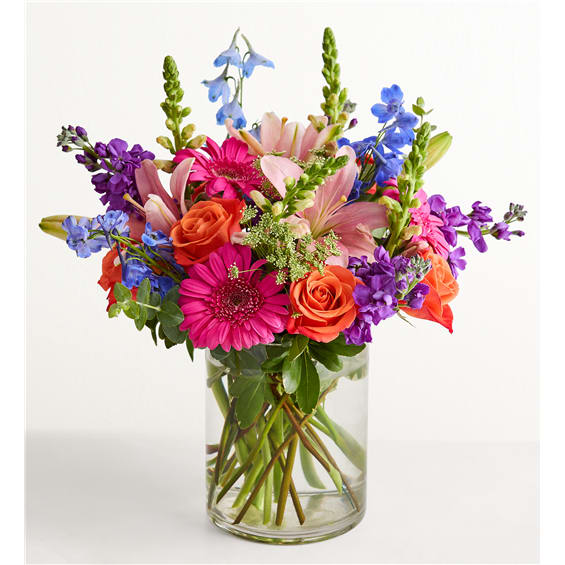 Mixed bouquet of pink, orange, and purple flowers in a clear glass vase