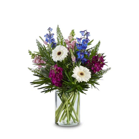 Mixed bouquet of blue, pink, and white flowers in a clear glass vase