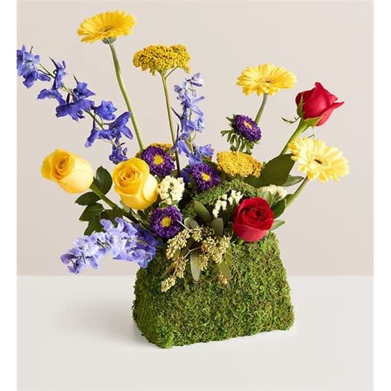 Mixed bouquet of roses, daisies, and blue flowers in a moss-covered container