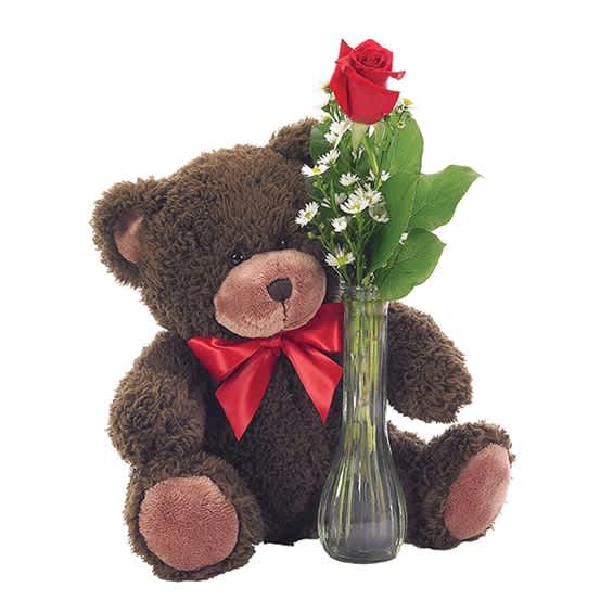Teddy bear beside a glass vase with red roses and small white flowers