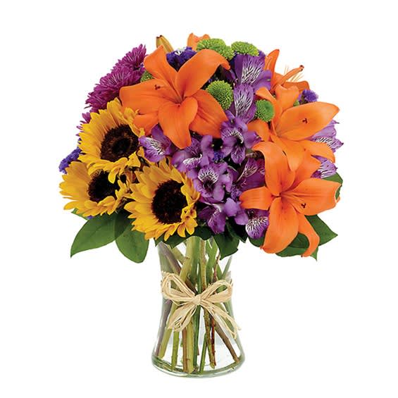 Bouquet of orange lilies, sunflowers, and purple flowers in a glass vase