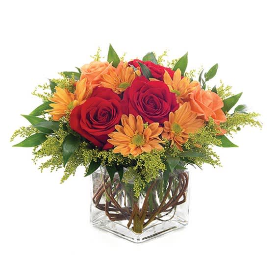 Red roses and orange daisies in a clear square vase