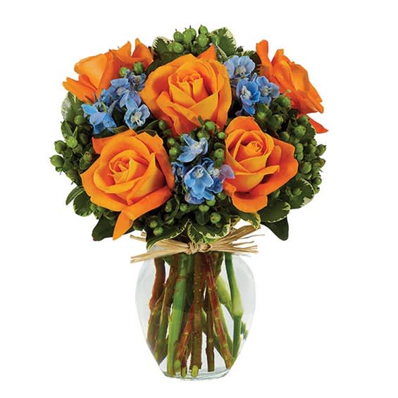 Bouquet of orange roses and blue flowers in a clear glass vase