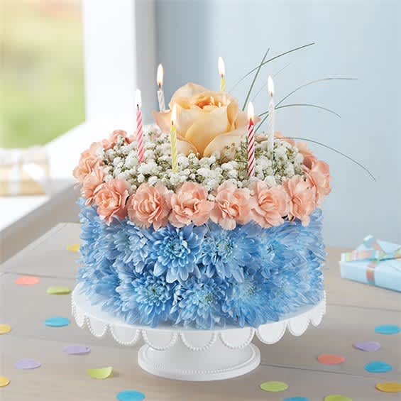 Cake-shaped floral arrangement with candles and pastel flowers on a pedestal