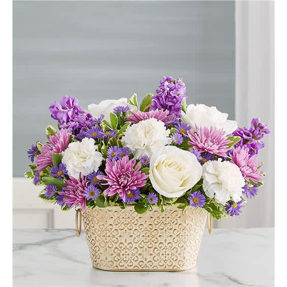 Purple, pink, and white flowers arranged in a decorative cream container