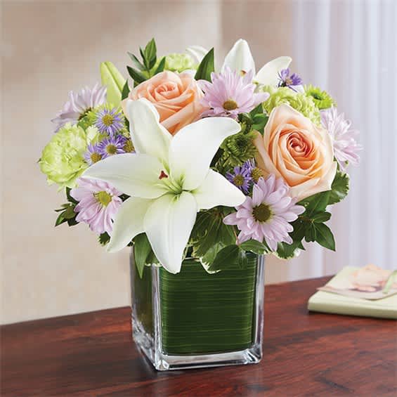 Bouquet of white lilies, peach roses, and lavender daisies in a square glass vase