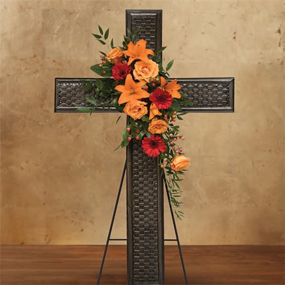 Floral cross arrangement with orange lilies, roses, and red daisies