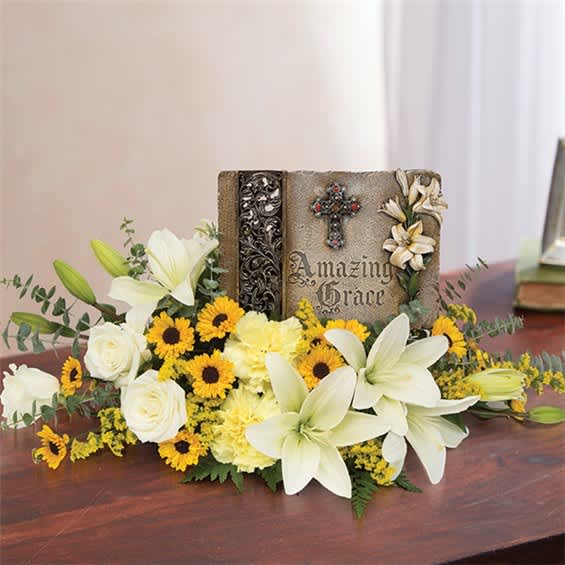 White lilies and yellow flowers arranged around a decorative memorial book