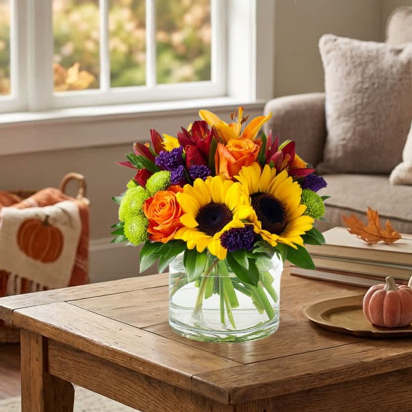 Bright mixed bouquet of sunflowers, roses, and mums in a clear glass vase