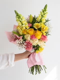 Handheld bouquet of yellow roses, lilies, and pink carnations wrapped in pink paper