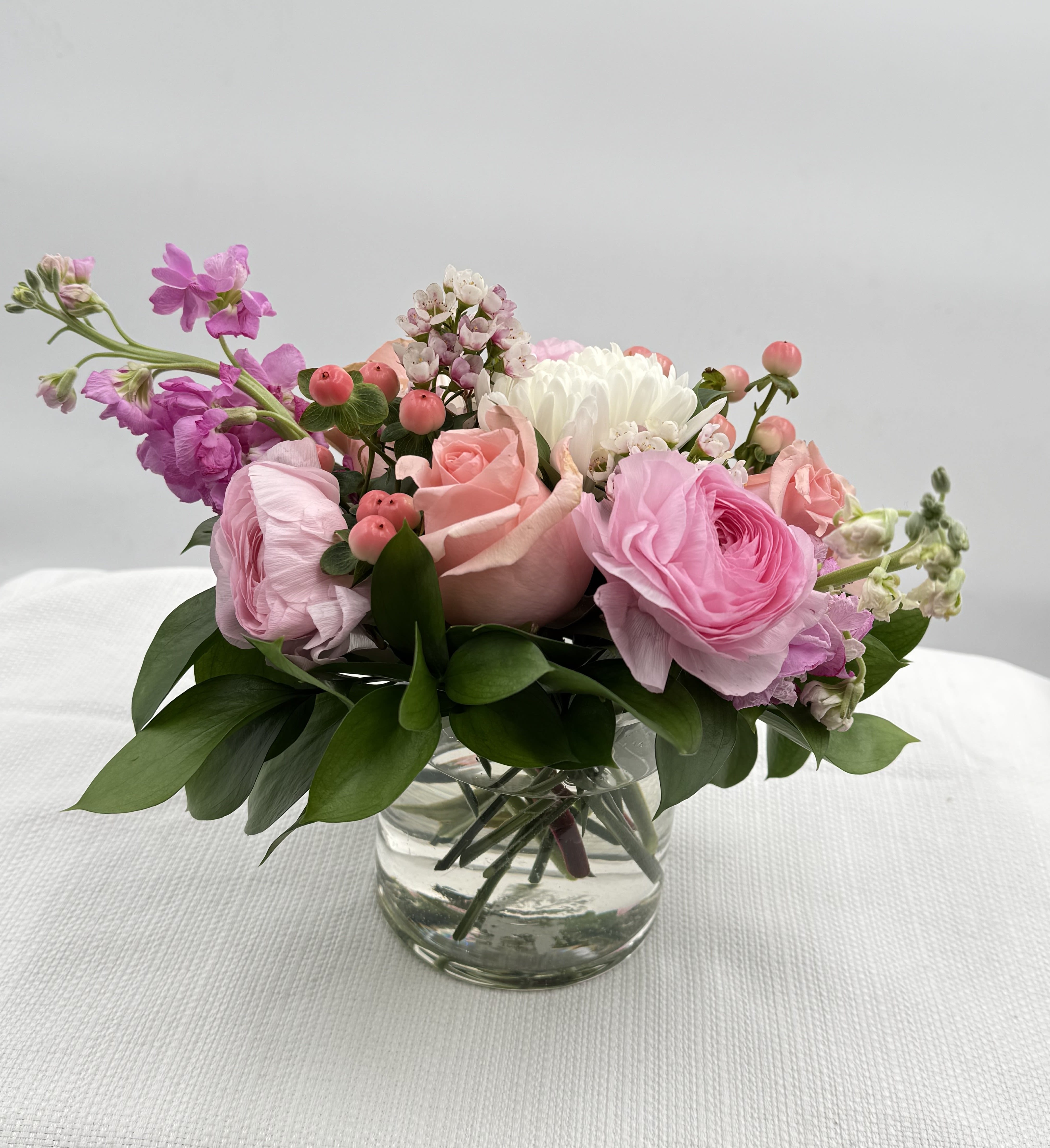 Low arrangement of soft pink and white roses and ranunculus in a clear glass vase.