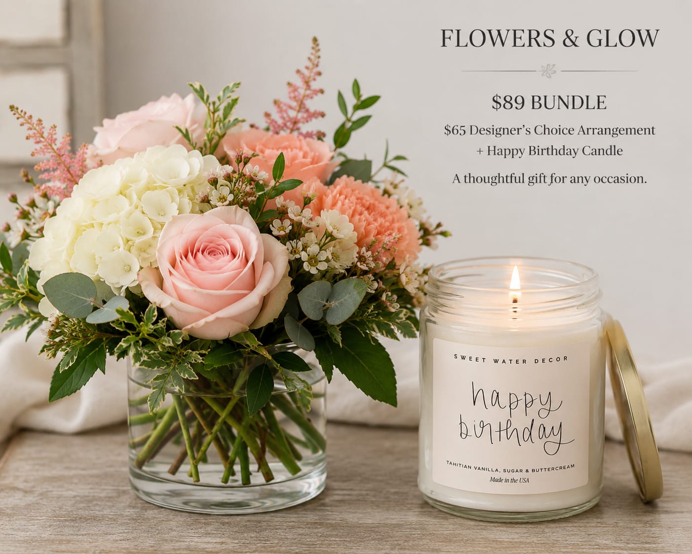 Pink and white flower arrangement in a glass vase beside a lit birthday candle.