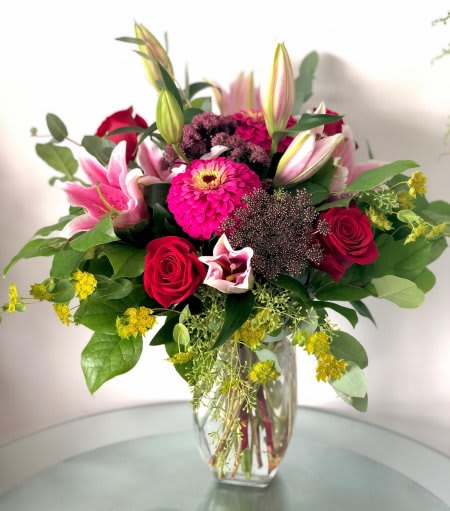Clear vase arrangement with pink lilies, bright pink blooms, and red roses