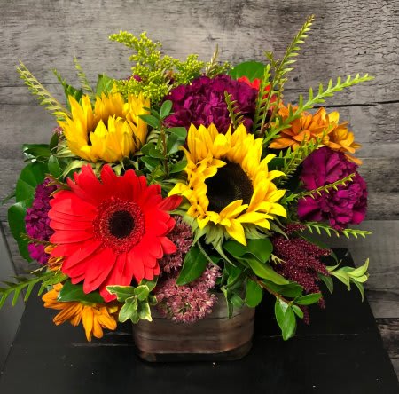 Bright mixed arrangement with sunflowers and red gerbera daisies in a rustic square container
