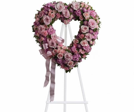 Heart-shaped pink rose wreath on a white stand with ribbon