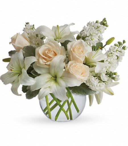 Low arrangement of white lilies and cream roses in a round clear glass vase