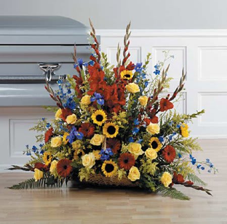 Large funeral spray with sunflowers, yellow roses, and red flowers in a basket base