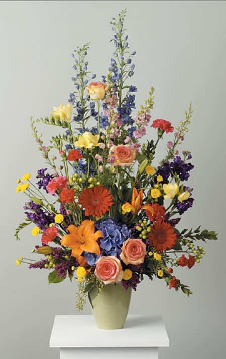 Tall mixed flower arrangement in a pale vase with orange, pink, yellow, and purple blooms