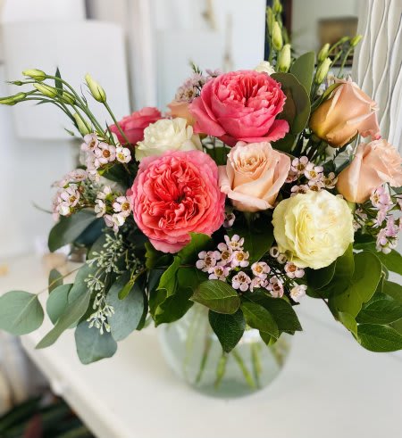 Mixed arrangement of pink and cream roses with small white blossoms in a clear glass bowl vase