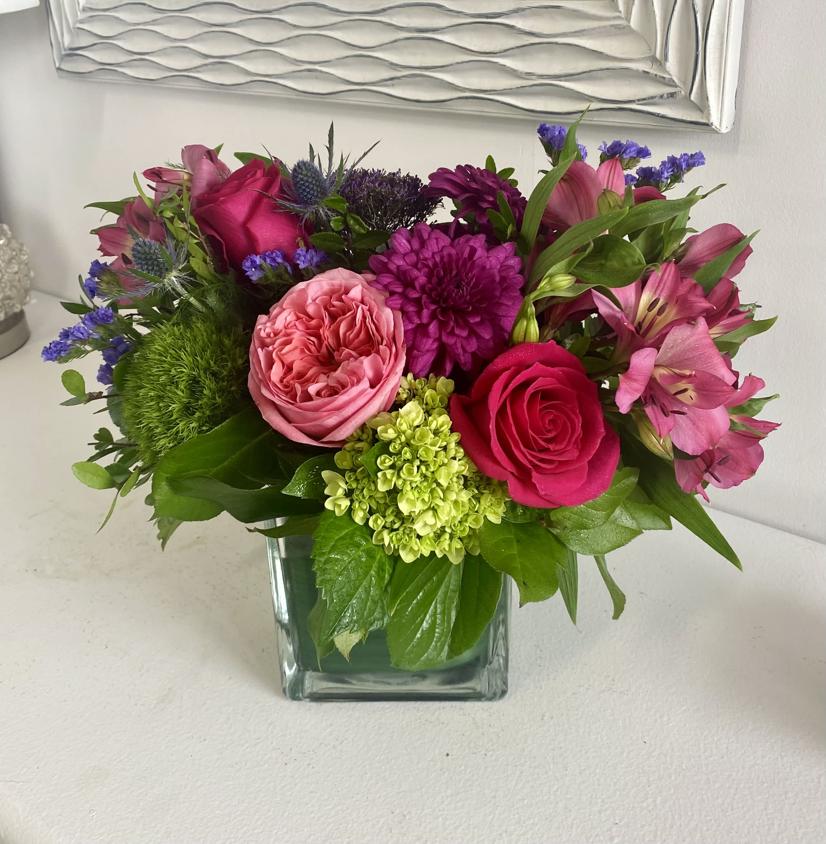 Pink and purple mixed flower arrangement in a square glass vase