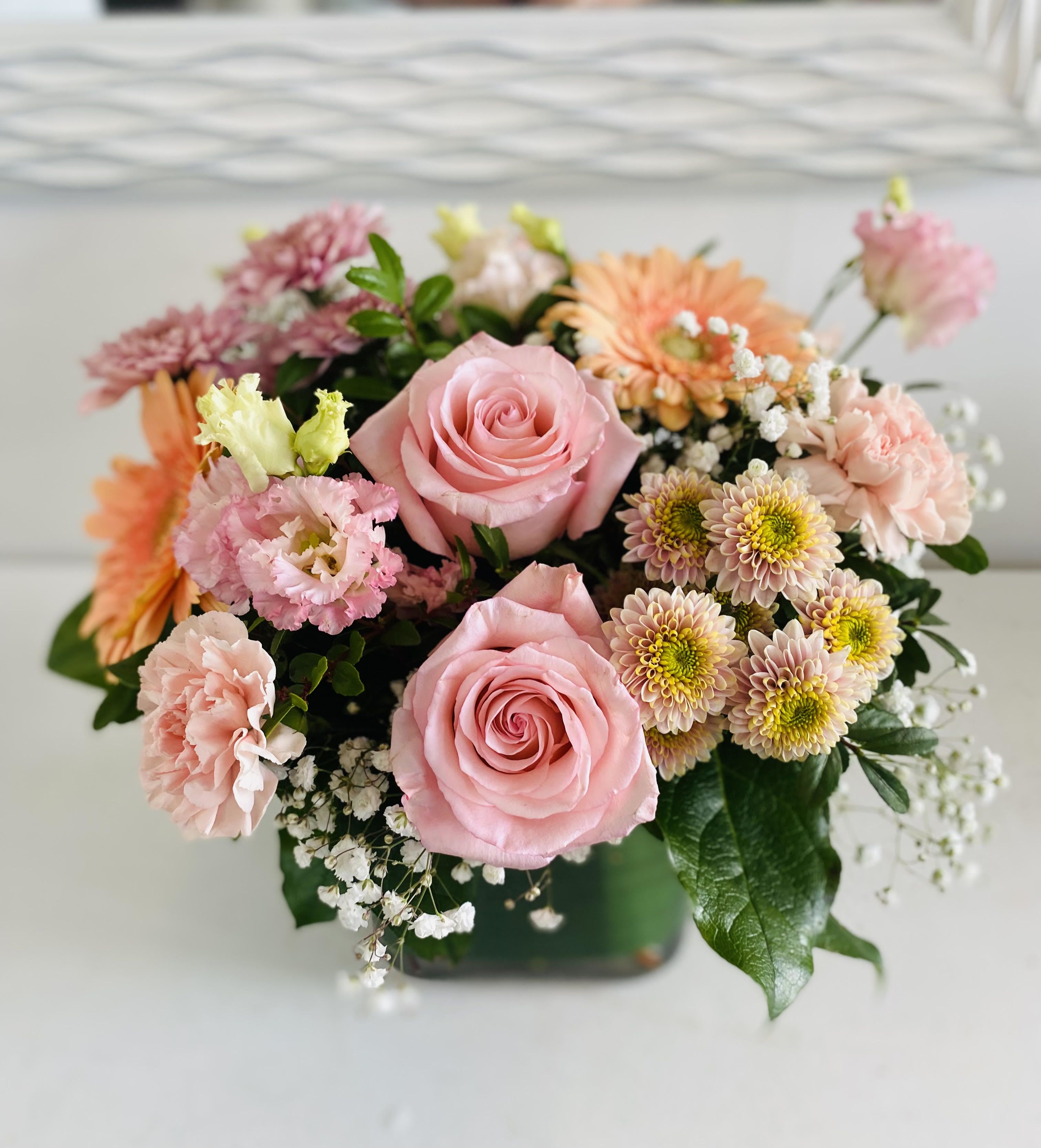 Pink roses and mixed pastel flowers arranged in a low square vase