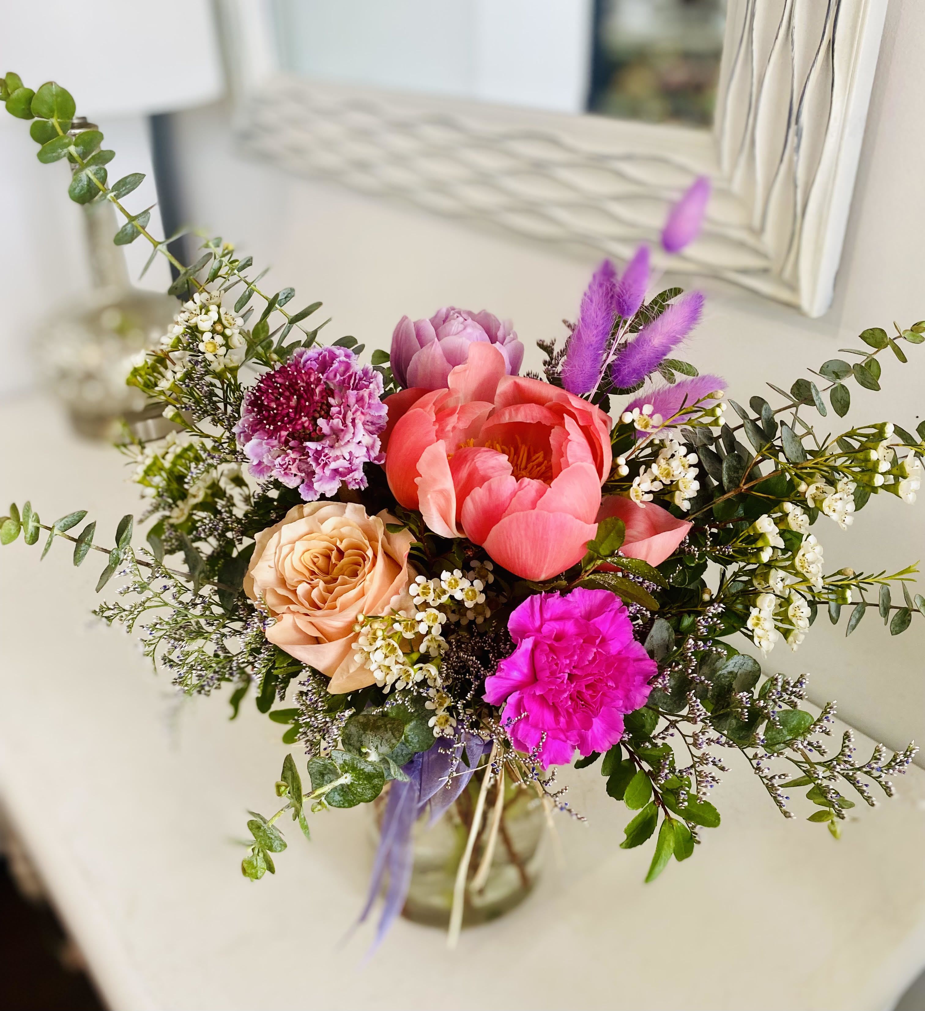 Mixed arrangement of pink peonies, roses, and carnations in a clear glass vase