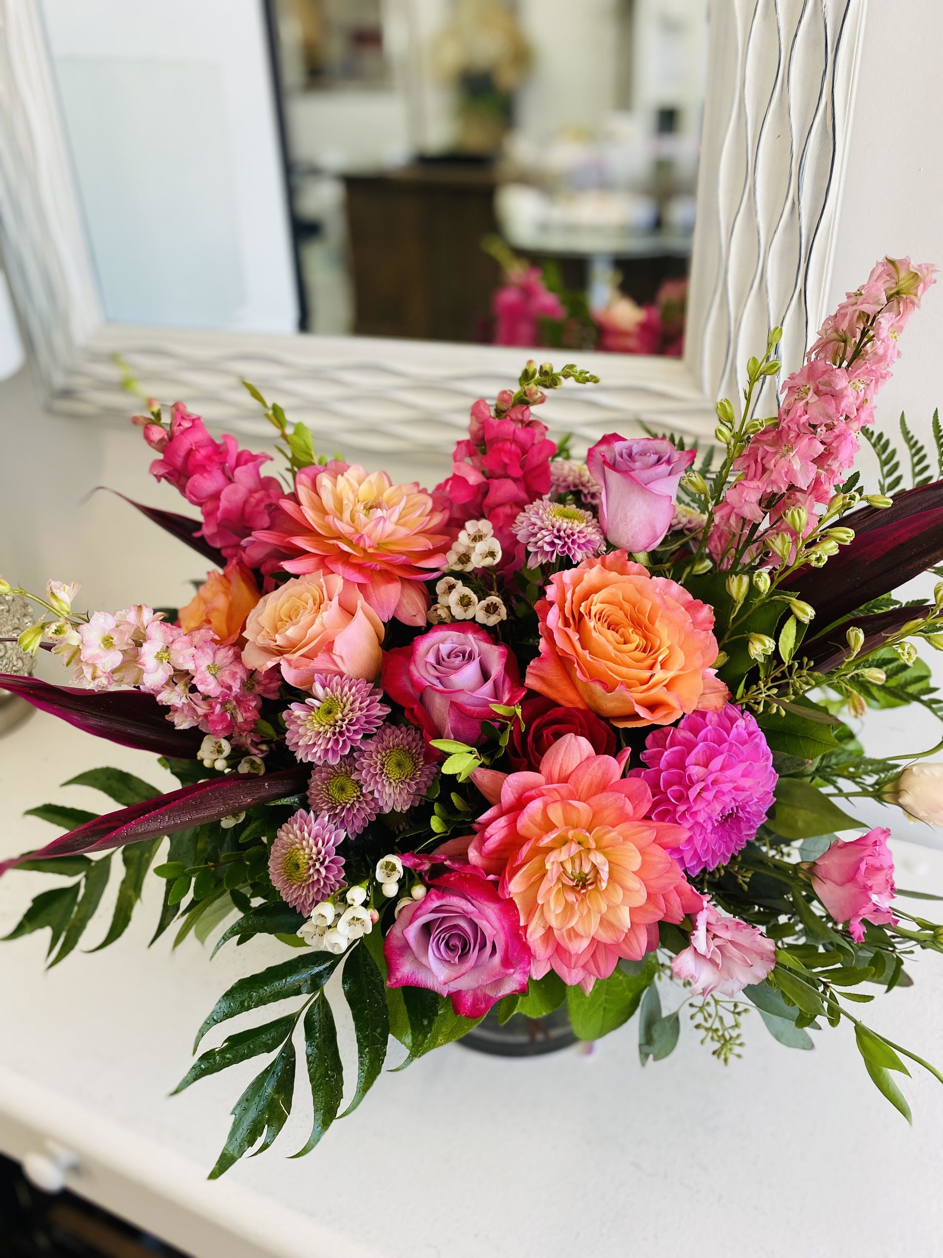 Bright arrangement of pink and orange dahlias, roses, snapdragons, and mums in a low glass vase