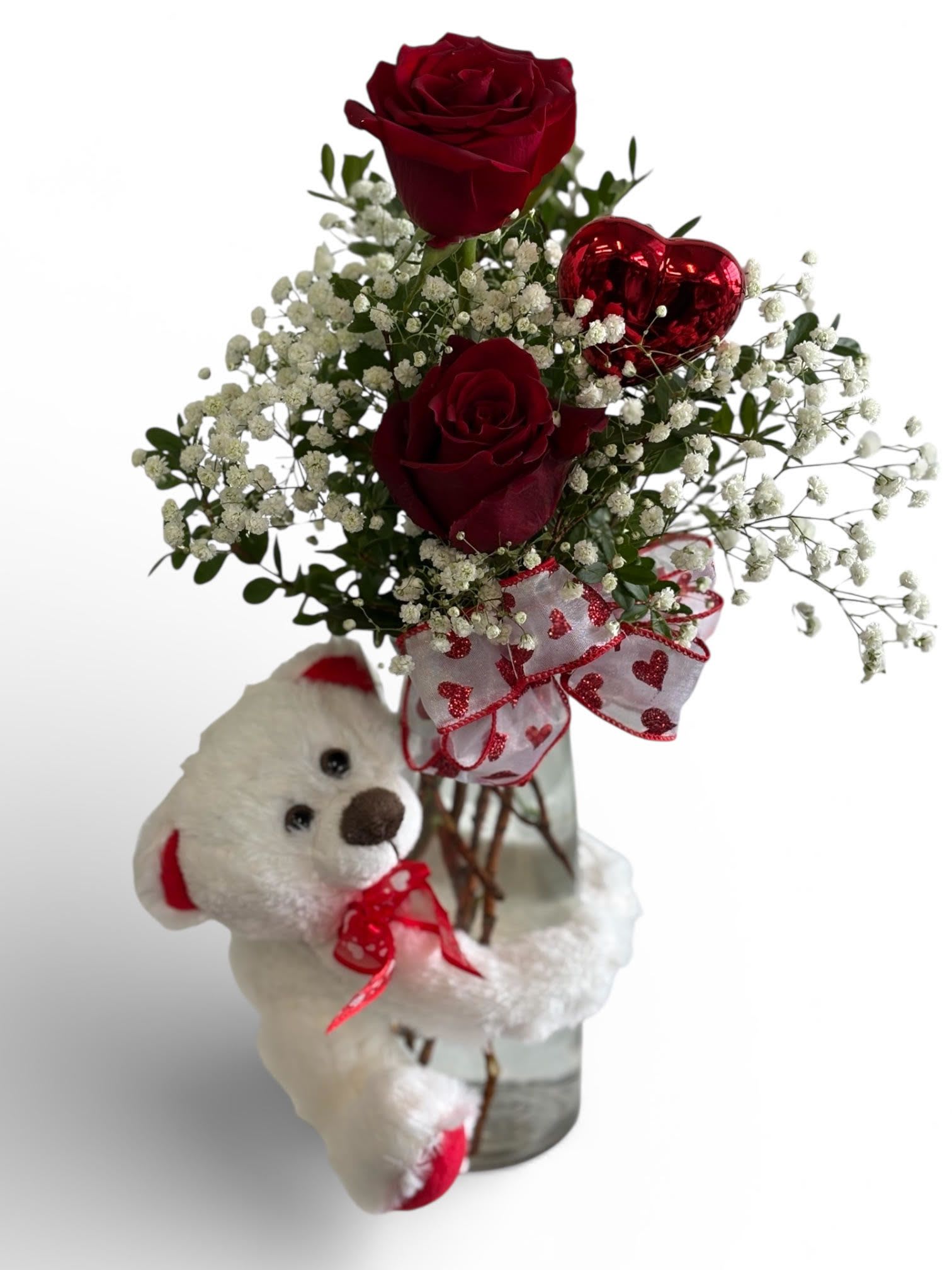 Small vase with red roses, baby's breath, heart pick, and a white teddy bear.