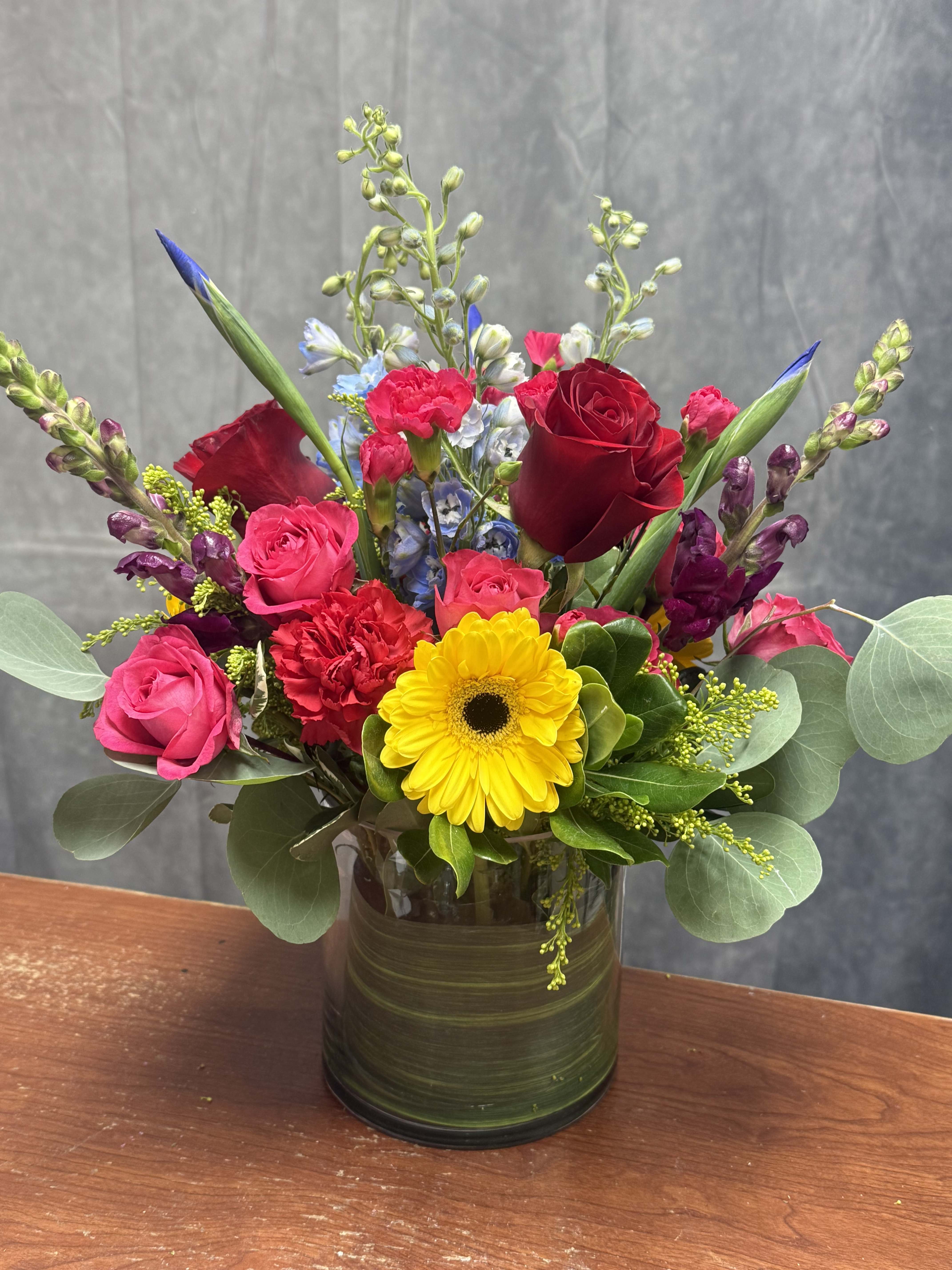 Mixed bouquet of roses, gerbera daisies, and snapdragons in a glass vase