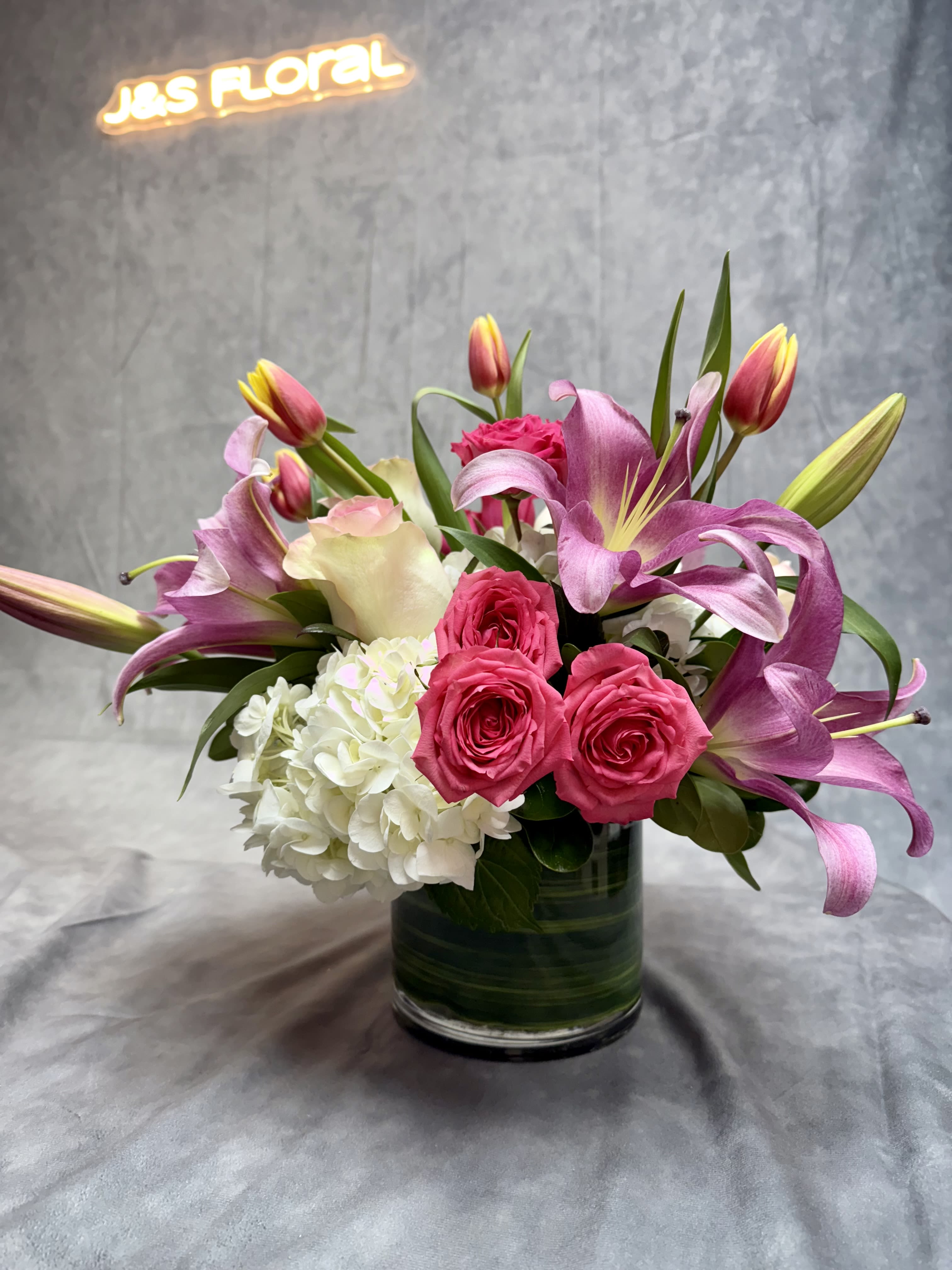 Pink lilies and roses arranged in a glass vase with white hydrangea.