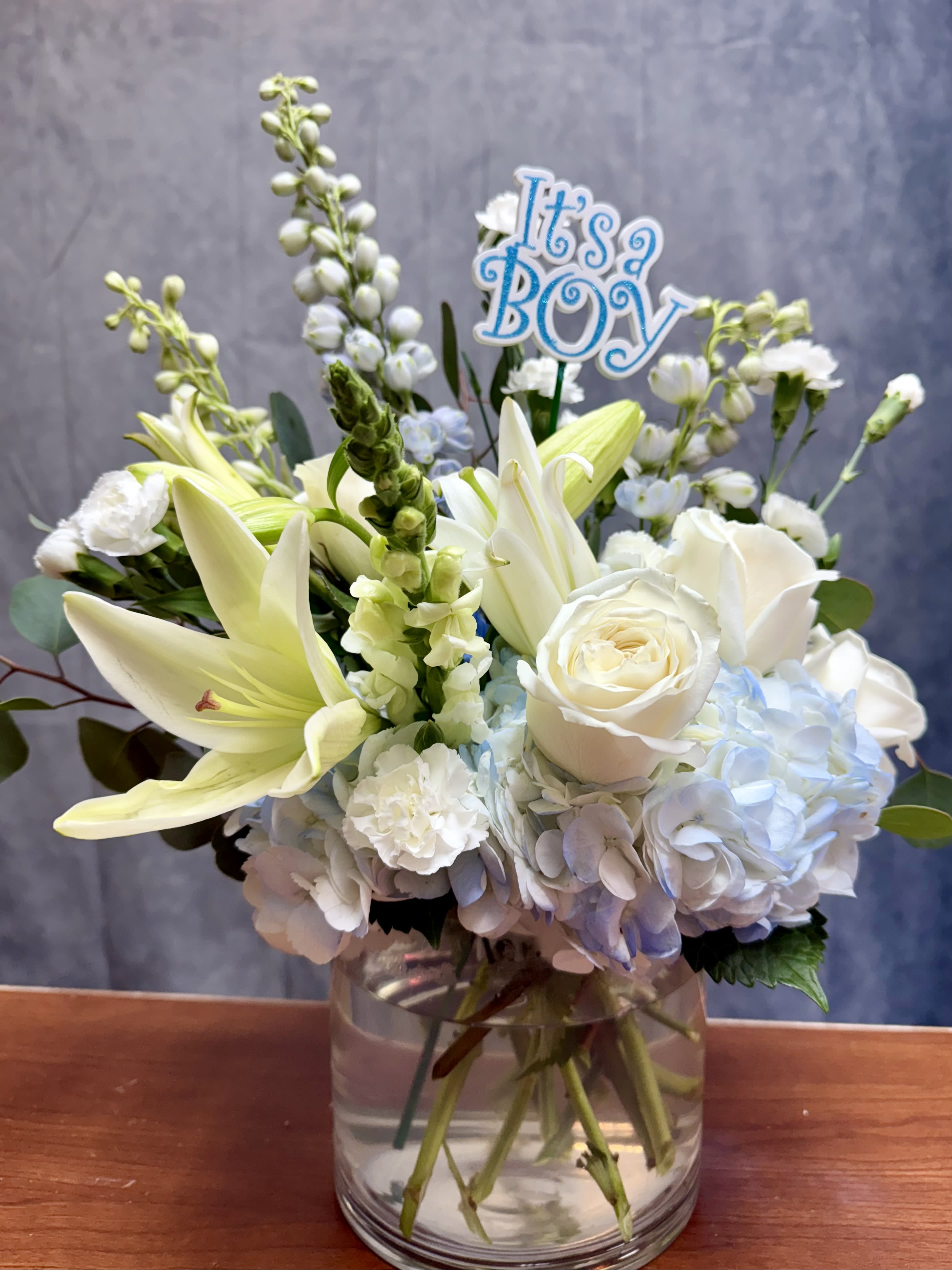 White and pale blue bouquet in a glass vase with an "It's a Boy" sign