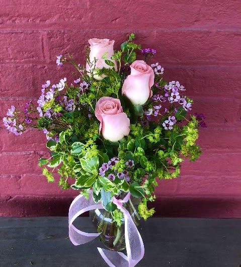 Pink roses in a glass vase with purple filler flowers and a ribbon