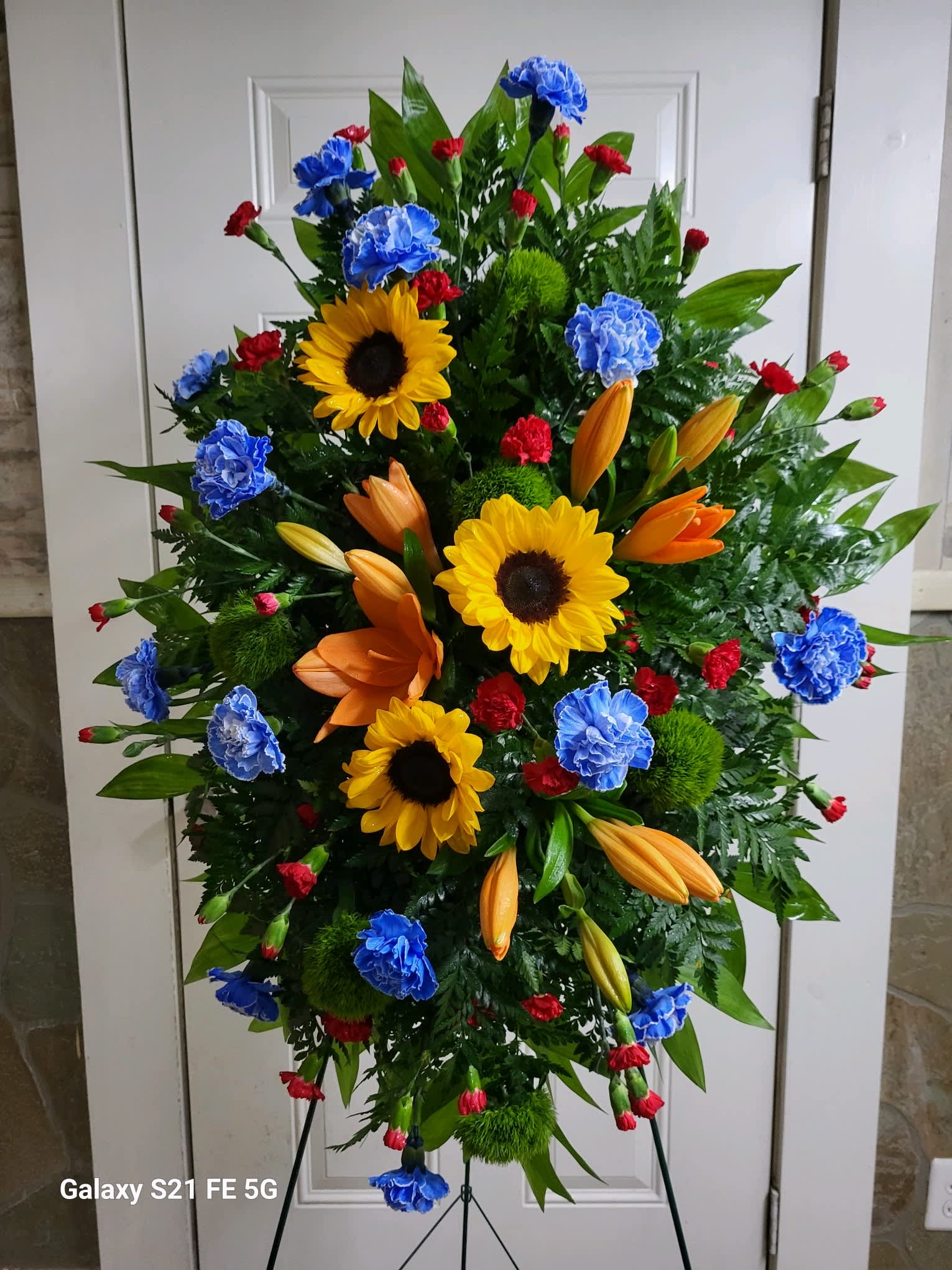 Standing floral spray with sunflowers, lilies, and carnations in bright colors
