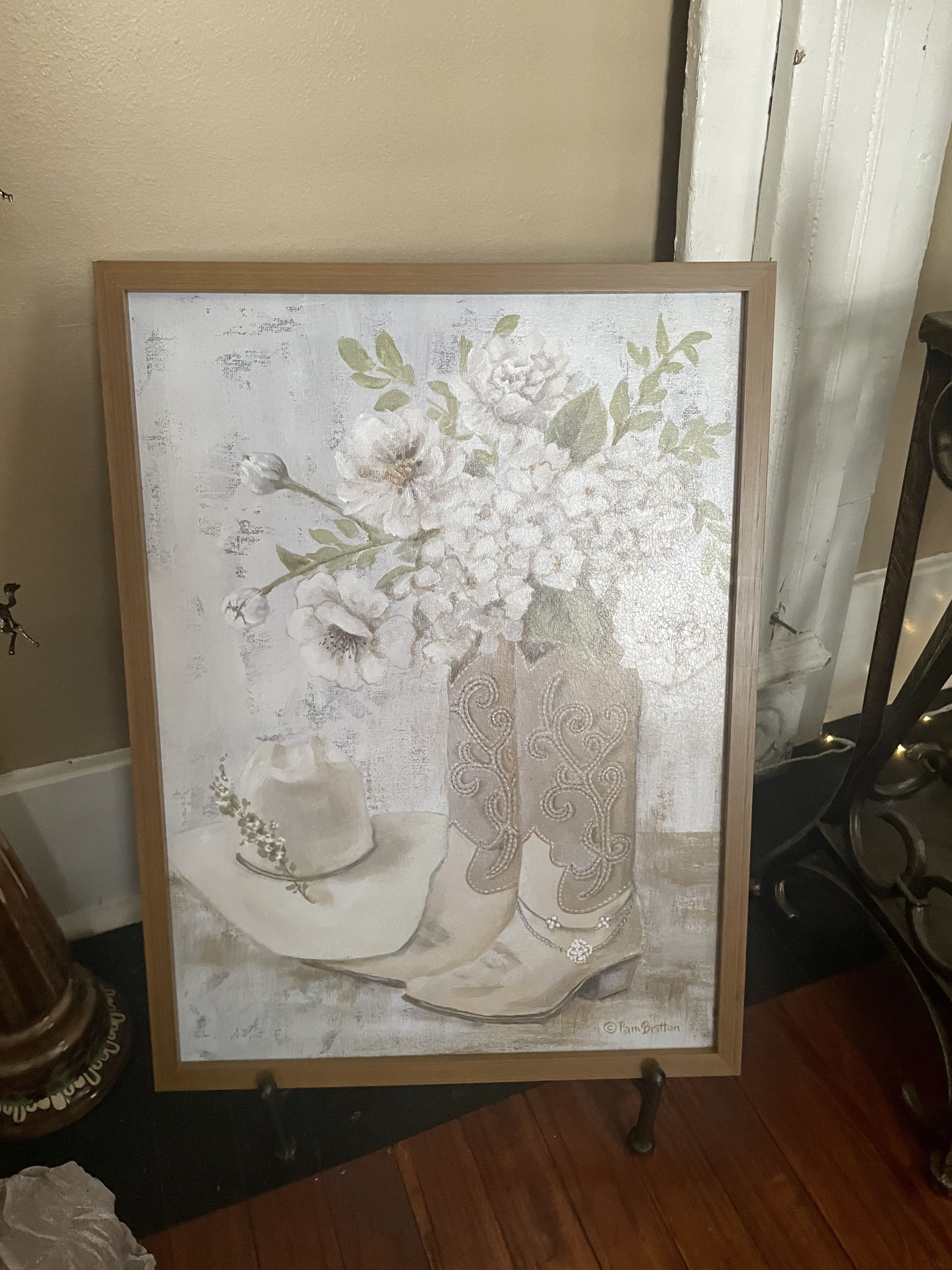 Framed artwork of white flowers in a vase beside a cowboy hat and boots